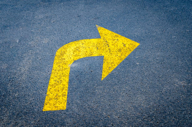 yellow arrow on black pavement pointing right - turning right imagens e fotografias de stock