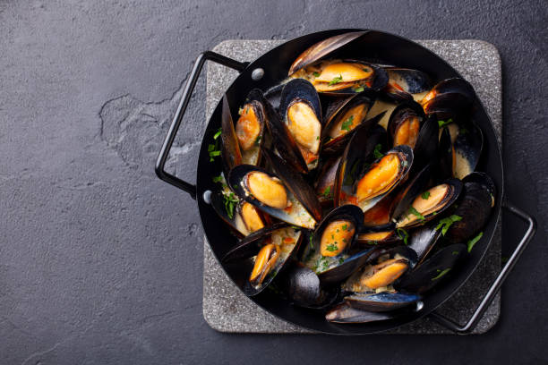 istock Mussels with herbs and sauce in black pan. Dark background. Copy space. Top view. 1215360470