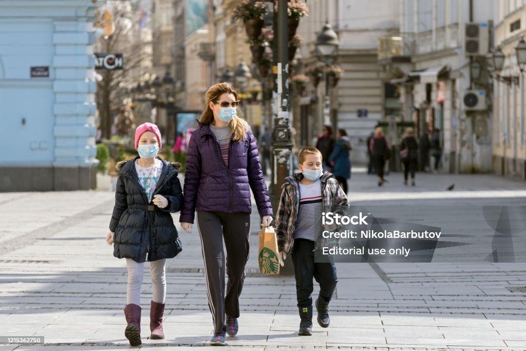 Madre y dos niños pequeños caminando por las calles de la ciudad usando máscaras faciales contra coronavirus. COVID - 19 pandemia. Vista de la calle en el centro de la ciudad - Foto de stock de Máscara protectora libre de derechos