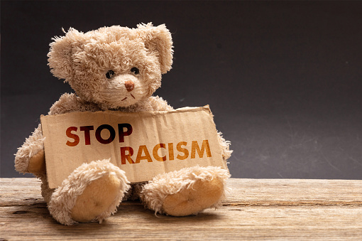 Stop racism. Poor homeless child begging. Teddy bear holding a cardboard sign. No to racism message