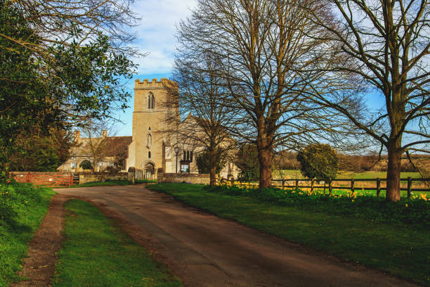 The pathway leading to the Church of St Andrew in Cotterstock, near Oundle in Northamptonshire, England in Spring, with yellow daffodil flowers lining the verge