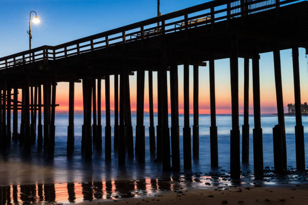 istock Ventura Pier at Sunset. Beach with rocks in foreground, smooth ocean; colored sky in background. 1215365959