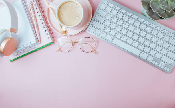 istock Flat lay of office feminine desk workspace with cup of coffee, succulent, laptop, empty notebook, headphones, keyboard, and golden eyeglasses on pink background. Top view. Copy space 1215367749