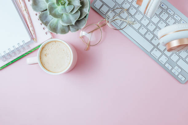 istock Flat lay of office feminine desk workspace with cup of coffee, succulent, laptop, empty notebook, headphones, keyboard, and golden eyeglasses on pink background. Top view. Copy space 1215367773