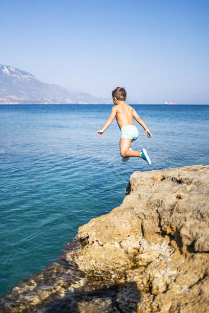 istock Little boy jumping from a rock into the sea 1215367955