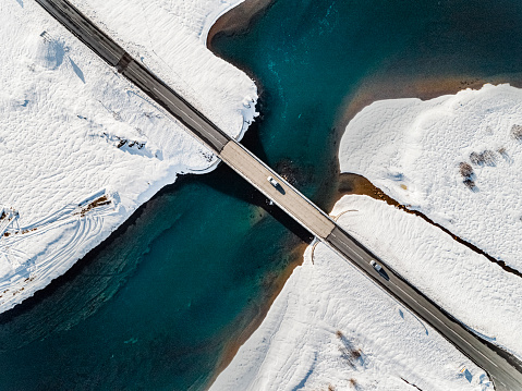 Aerial view on a sunny winter’s day of a bridge connecting two roads over a river in snowy nature