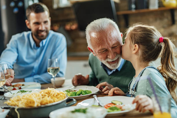 kochająca wnuczka całuje dziadka podczas lunchu przy stole. - dining table child grandparent grandchild zdjęcia i obrazy z banku zdjęć