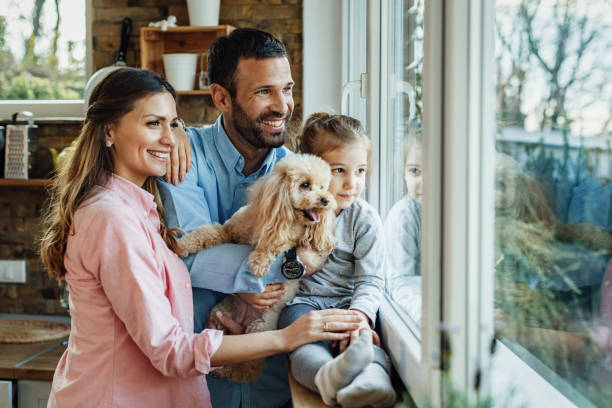 famiglia felice con un cane che guarda attraverso la finestra di casa. - guardare fuori foto e immagini stock