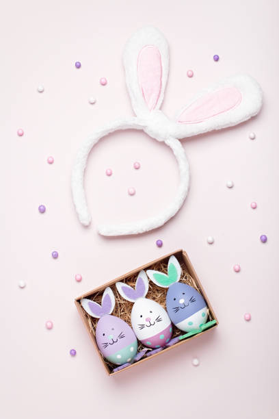 istock Funny kawaii bunny eggs and bunny rabbit ears for kids on pastel pink table top, Easter holiday concept. Easter decoration and set for creative activity for kids with crayons and notebook flat lay 1215371114