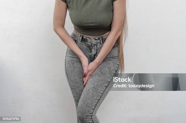 Young Slim Girl In Jeans Holds Hands Pressed Between Her Legs Stock Photo - Download Image Now