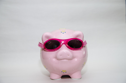 Pink piggy bank with sunglasses on white background