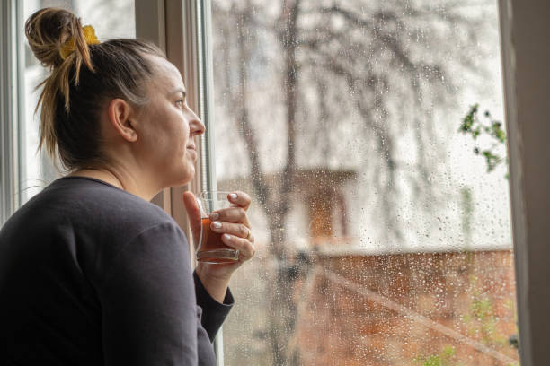 istock woman looking through window on rainy day and drinking tea 1215377969