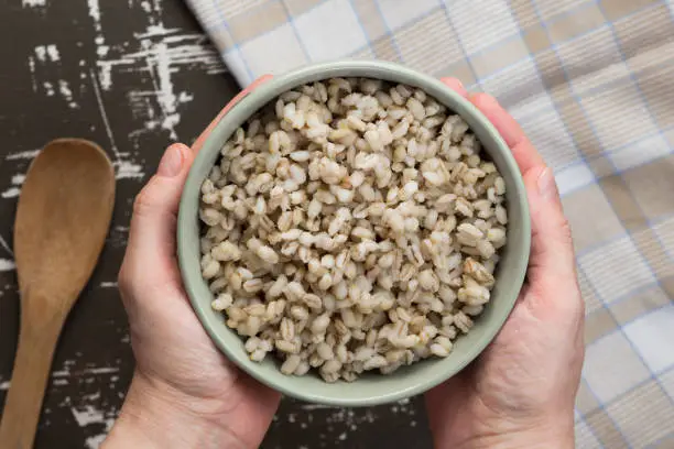 Top view of woman hands holding bowl with pearl barley porridge on wooden surface