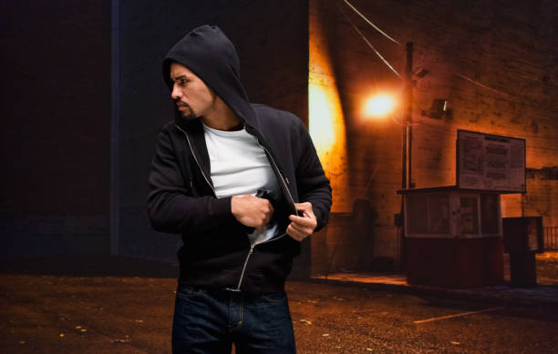 Pacific islander ethnicity young male criminal wearing sweatshirt and holding weapon and using handgun Waist up of pacific islander ethnicity young male criminal wearing sweatshirt who is horror who is violence and holding weapon and using handgun man holding gun at night in the city stock pictures, royalty-free photos & images