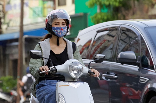 Woman in a protective mask rides a scooter on the street.