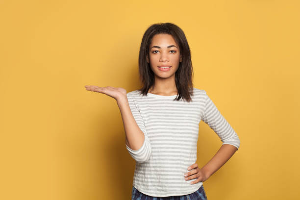 istock Happy black woman student  with empty open hand on yellow background 1215386247