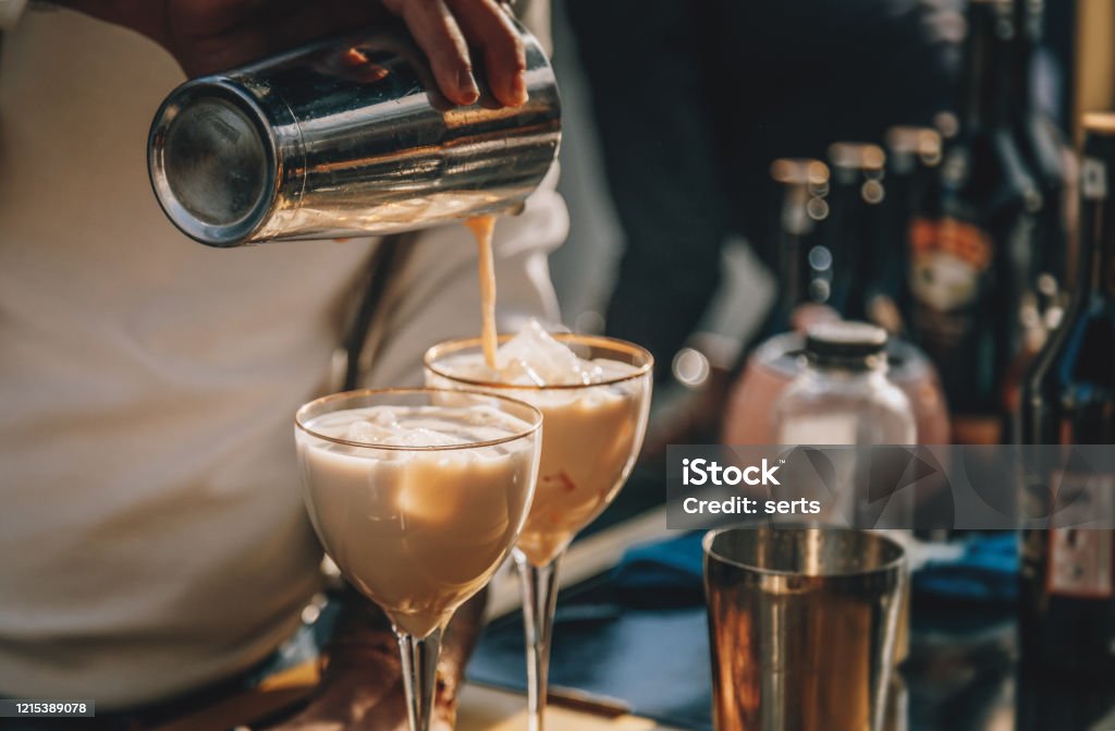 Bartender preparing  Irish Cream Liqueur cocktail with shaker Close up male bartender hands making Baileys cocktail with ice and pouring to glass from bar shaker Cocktail Stock Photo