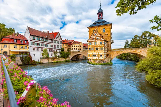 Bamberg city in Germany. Town hall building in background with blue cloudy sky.  Architecture and travel in Europe. Flowing river in foreground.