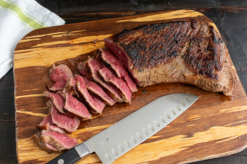 Partially sliced grilled beef roast on a wood cutting board