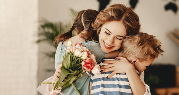 Little children congratulating and hug mother in kitchen Happy Mothers Day! Children boy and girl congratulate smiling mother, hugs her  and give her flowers   bouquet of tulips during holiday celebration in kitchen at home bunch of flowers photos stock pictures, royalty-free photos & images