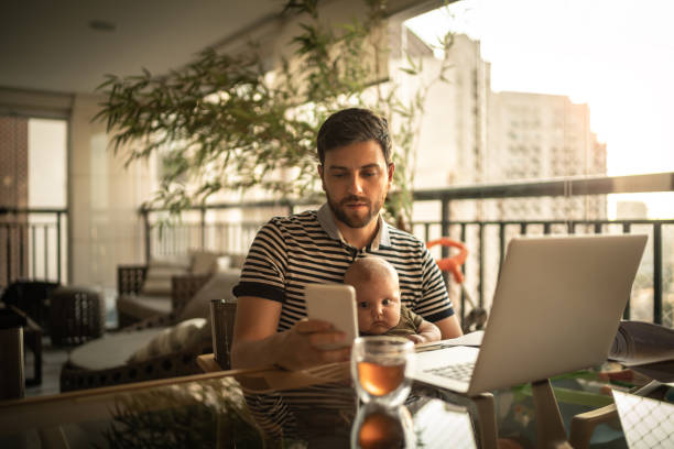 Man holding his newborn baby son and working with laptop at home Man holding his son and working with laptop at home man work from home baby stock pictures, royalty-free photos & images