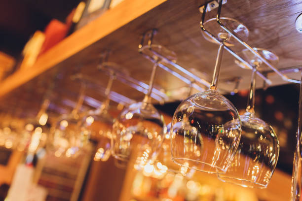 istock Closeup many upside down empty clear transparent crystal upturned wine glasses hanging in straight rows on brown wooden shelf, rack, showcase, stainless steel railing in bar, cabinet. 1215414833