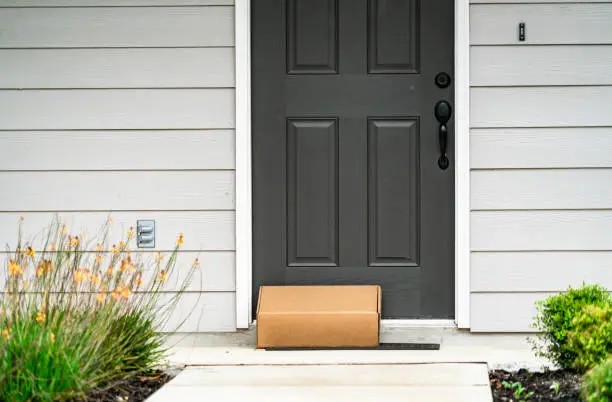 Package Delivery on Doorstep during Covid-19 pandemic , perfect suburb home with grey front door and cardboard box on door step