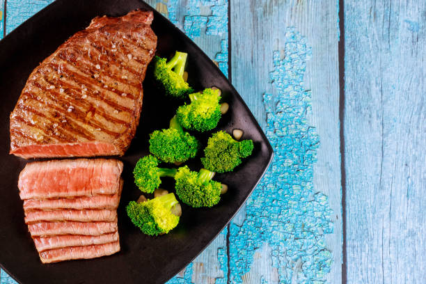 Medium rare beef sirloin with broccoli on black plate.