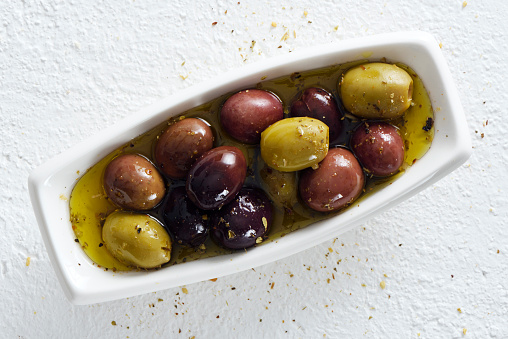 Green and black olives with oil and spices on a white background