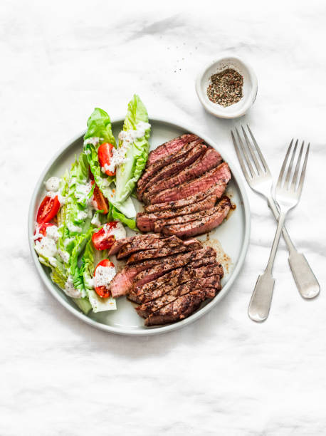 istock Beef steak and romaine cherry tomatoes yogurt dressing salad on a light background, top view 1215442239