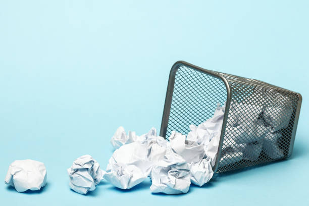 istock Overturned trash can with crumpled paper balls on a blue background. Closeup copy space 1215445196
