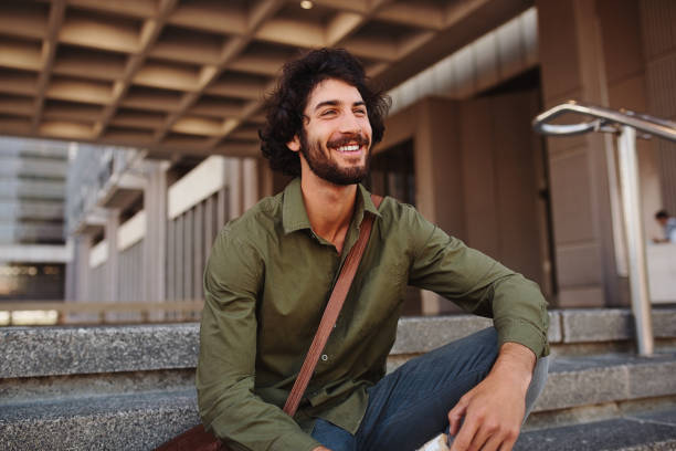 istock Handsome young man sitting on stairs while looking away 1215449821