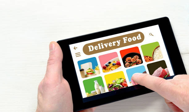 istock Male hands holding tablet computer with app delivery food on screen above white desk. 1215453662
