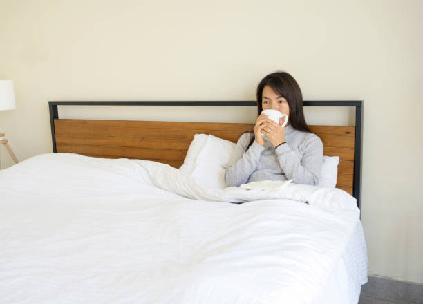 istock Asian woman sit in bed drinking hot tea 1215454040