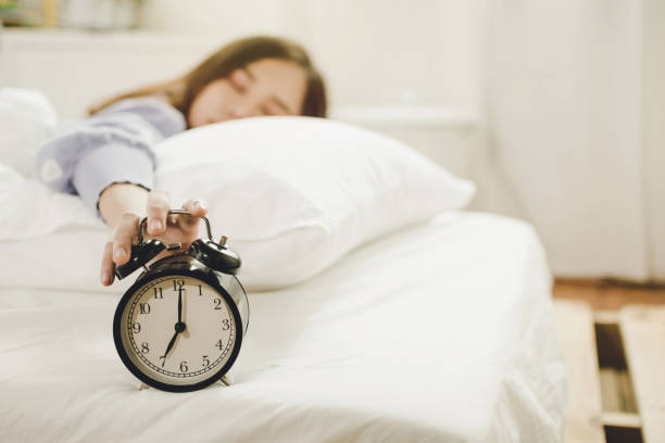 young asian woman sleeping on bed pressing snooze button on black vintage alarm clock at seven o'clock morning in bed room at home, lifestyle, good morning, healthy sleep and joyful weekend concept joven mujer asiática durmiendo en la cama presionando botón de repetición en negro reloj despertador vintage a las siete de la mañana en la habitación de la cama en casa, estilo de vida, buenos días, sueño saludable y concepto de fin de semana alegr