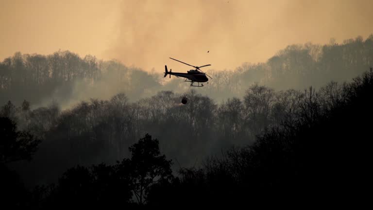 Silhouette Helicopter with firefighters throwing water to fire in the wildfire forest