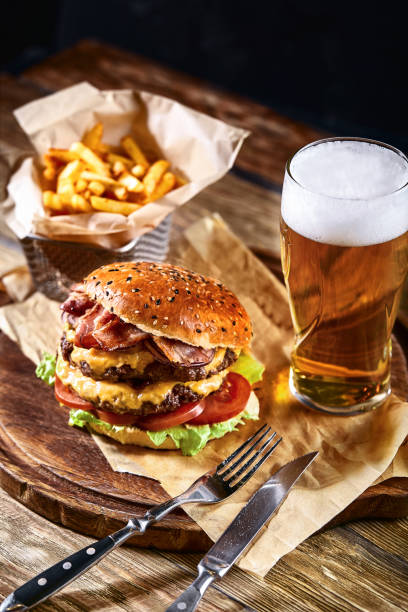 delicious hot spicy black burger with chili pepper and glass of beer on cutting board on white wood table - close to food and drink yummy food imagens e fotografias de stock