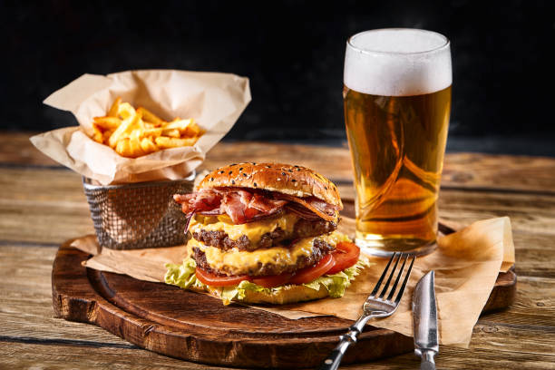 delicious hot spicy black burger with chili pepper and glass of beer on cutting board on white wood table - close to food and drink yummy food imagens e fotografias de stock