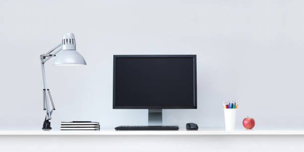 Clean white office desk in with computer and lamp.