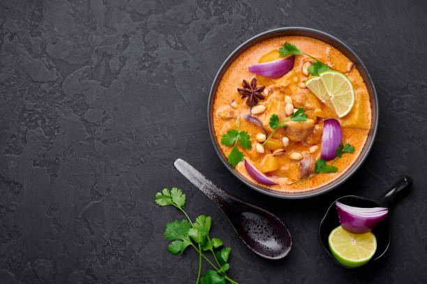 istock A Chicken Massaman Curry in black bowl at dark slate background. Massaman Curry is Thai Cuisine dish with chicken meat, potato, onion and many spices. Thai Food. Copy space. Top view 1215468741