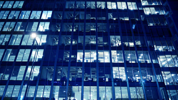 istock Pattern of office buildings windows illuminated at night. Lighting with Glass architecture facade design with reflection in urban city. 1215470446