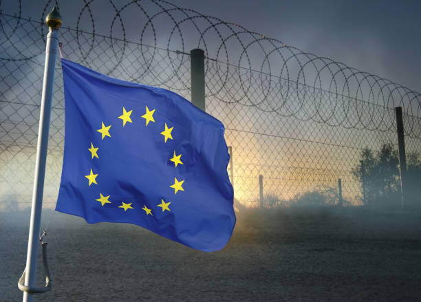 istock Barbed and razor wire on a fence with EU flag. 1215474298