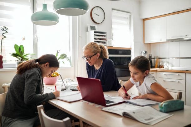 homeschooling - mãe ajudando suas filhas a terminar a lição de casa durante a quarentena do coronavírus - equipamento de telecomunicação - fotografias e filmes do acervo