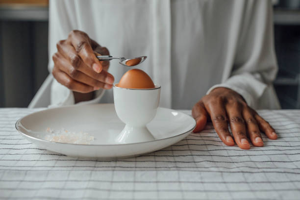 Hands of unrecognisable woman breaking boiled egg for breakfast.