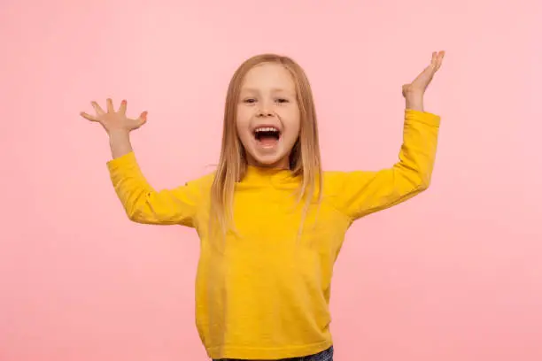 Happy carefree child emotions. Energetic joyful adorable little girl raising hands and screaming with happiness, rejoicing victory, laughing at joke. indoor studio shot isolated on pink background