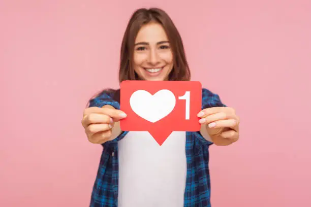 Photo of Portrait of happy blogger girl in checkered shirt smiling and showing like icon, heart button