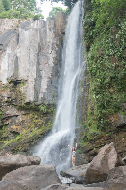 istock Woman opens arms front of waterfalls 1215486971