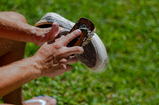 Young adult washing and brushing his sneakers with soap and water in the garden of the house. 
A form of hygiene and conservation of footwear. Right after this wash, the shoe should be drying in the sun for better durability