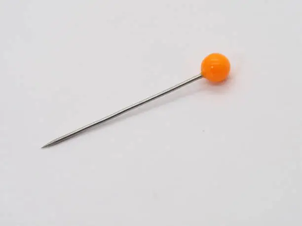 An orange hat pin standing upright on a white background