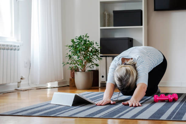 Senior woman following tutorial online and exercise at home during isolation for Covid - 19 at home stock photo